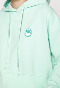 Miętowa bluza z kapturem, wykonana z miękkiej bawełny, z kieszenią typu kangur, sznurkiem w kapturze oraz okrągłym logo z napisem "RINKO" w kolorze białym.