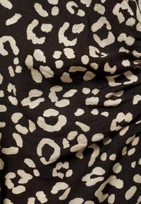 Crni materijal s sjajnom završnom obradom koji prikazuje bež uzorak leoparda, ističući raznolike oblike i teksture po cijeloj površini.