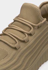 Μπεζ πλεκτό αθλητικό παπούτσι με χοντρές υφασμάτινες κορδόνια που περνούν μέσα από θηλιές, υφασμάτινη γλώσσα με υφή και ραβδωτή σόλα.