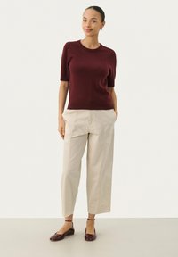 Top in magenta a maniche corte abbinato a pantaloni beigi plissettati e scarpe burgundy. L'insieme presenta una vestibilità rilassata e una consistenza morbida.
