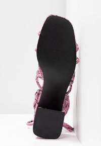 Sandale à talon haut tressée rose avec une semelle en caoutchouc noire. Présente des fines lanières et un talon carré. Empeigne texturée avec une finition à motifs.