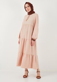 Blush pink maxi kjole med lagdelt design, lange ballonærmer og rund halsudskæring. Har en frynse-detail med snøring foran.