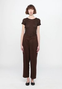 Brown mesh short-sleeve top and high-waisted, loose brown trousers. Simple design, smooth texture, and flat black shoes.