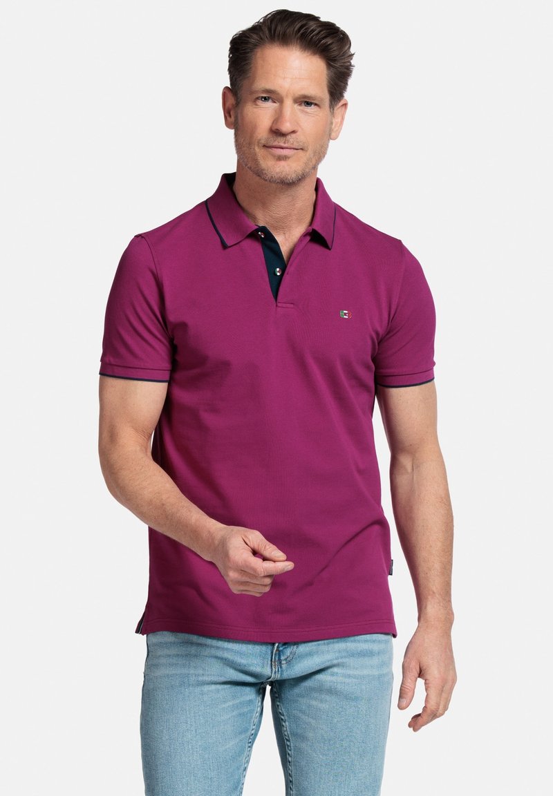 Polo shirt magenta avec un col foncé, à manches courtes et un petit logo sur la poitrine. Fabriqué en tissu lisse et texturé.