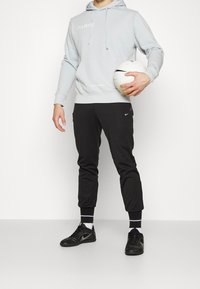 Sudadera gris con capucha con el texto "PARÍS", pantalones deportivos negros con el logo de Nike y zapatillas deportivas negras; sosteniendo un balón de fútbol blanco.
