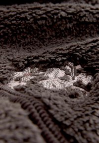 Aksominė tamsiai ruda medžiaga su tekstūruota paviršiumi. Puošniai išsiuvinėtos šviesiai pilkos gėlės, demonstruojančios gylį ir švelnumą.