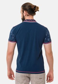 Marineblaues Poloshirt mit gemusterten kurzen Ärmeln, roten Akzenten am Kragen und an den Ärmeln sowie einer einfarbigen Rückseite.