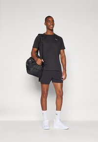 Svart atletisk t-shirt och shorts i lättviktsmaterial, med en logotyp. Kombineras med vita sneakers och en svart sportväska.