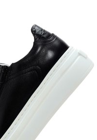 Sneaker in pelle nera con una finitura testurizzata, suola in gomma bianca e dettaglio della cerniera laterale. Il design presenta una silhouette elegante e moderna.