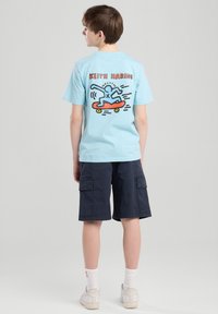 T-shirt di cotone azzurra chiara con un design colorato di Keith Haring sul retro, con dettagli in rosso e nero. Abbinata a pantaloni cargo scuri.