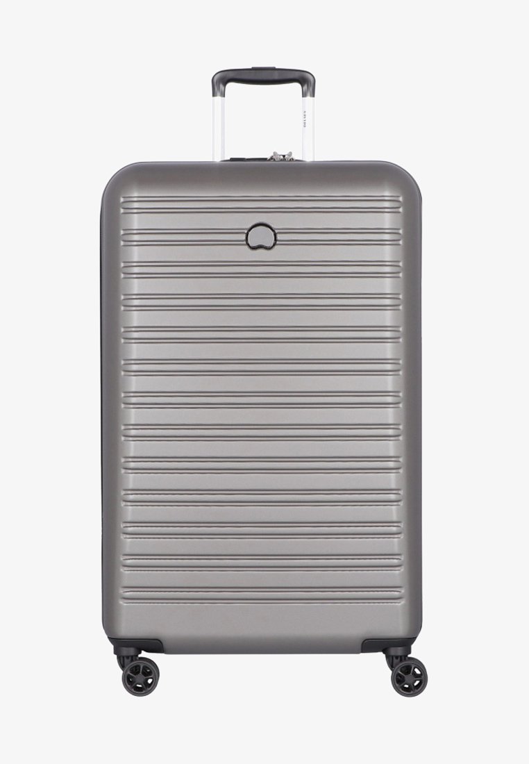 Valise rigide argentée avec des rainures horizontales, poignée télescopique et quatre roues pivotantes, vue de face.