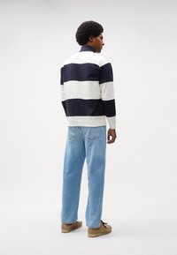 Polo a righe blu navy e bianche con maniche lunghe e colletto alto, abbinato a jeans a gamba dritta blu chiaro e scarpe marroni.