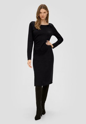 Zwarte jurk met lange mouwen en een aansluitende pasvorm, met een ronde halslijn en rimpeldetail bij de taille. Gepaard met zwarte kniehoge laarzen.