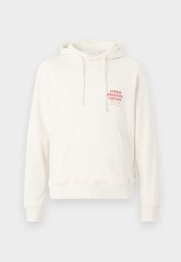 White hoodie made of soft fabric with a front pocket, featuring a red printed label reading "STUDIO ORIGINALS EDITION." Drawstring hood.