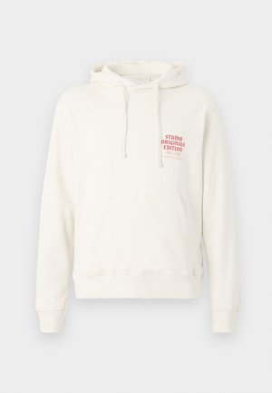 White hoodie made of soft fabric with a front pocket, featuring a red printed label reading "STUDIO ORIGINALS EDITION." Drawstring hood.