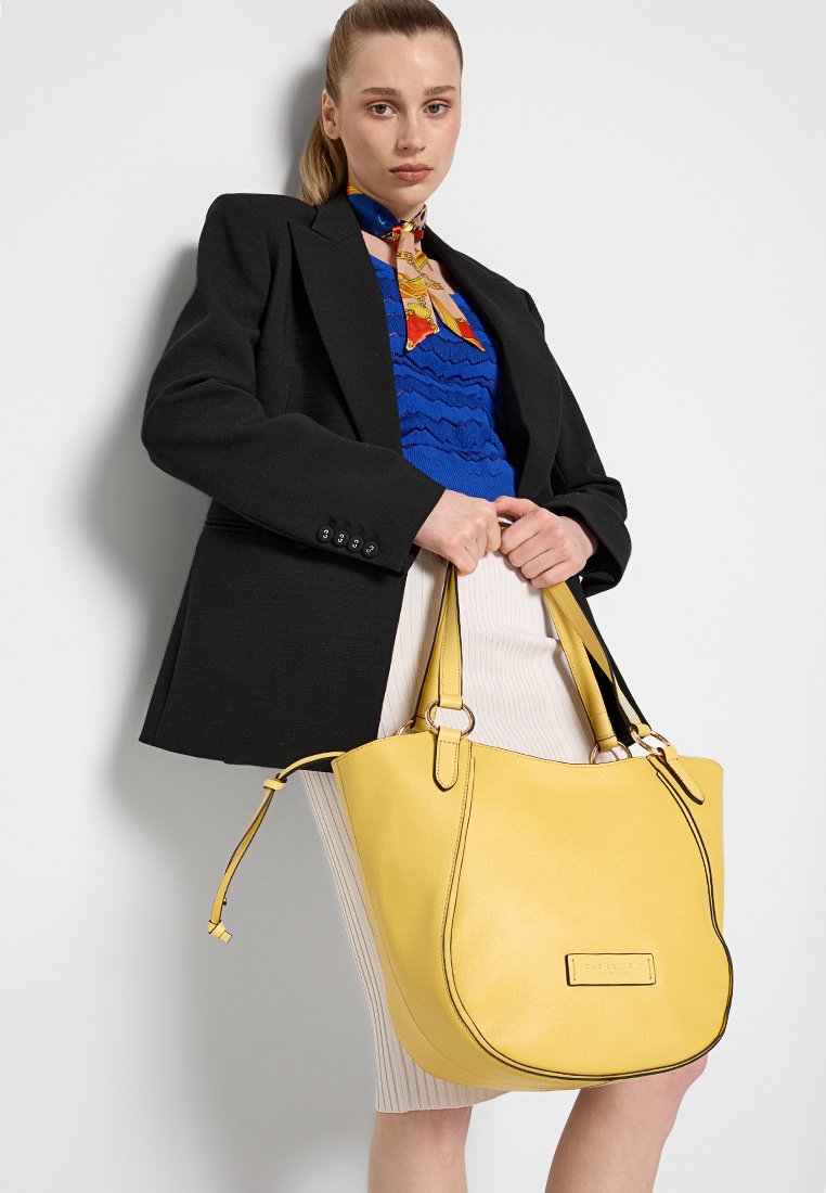 Grande borsa in pelle gialla con cuciture a contrasto. Presenta una forma arrotondata, doppi manici e un dettaglio logo rettangolare.