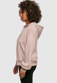 Lys rosa hettegenser med avslappet passform, snøring i hetten, ribbestrikkede ermer og kant. Mykt stoff med minimale detaljer.