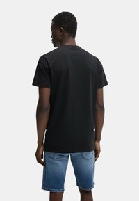 Maglietta nera a maniche corte realizzata in tessuto morbido, con scollatura girocollo classica. Indossata con pantaloni corti in denim chiaro e rovinati.