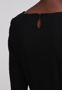 Vestido negro texturizado con escote redondo, abertura en forma de ojo de cerradura en la parte posterior y cierre con botón.