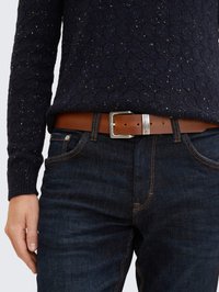 Brauner Ledergürtel mit silberner rechteckiger Schnalle, getragen über dunklen Denim-Jeans, kombiniert mit einem marineblauen Strickpullover mit strukturiertem Muster.