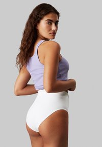 High-waisted white brief and lavender ribbed tank top; smooth texture, snug fit, and logo accent on the waistband.
