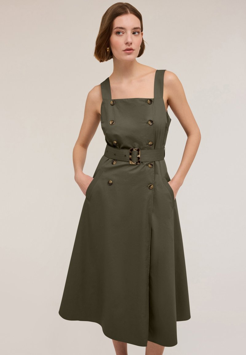 Olivgrön klänning med fyrkantig halsringning, breda axelband, dubbelknäppt front, midjebälte, två sidofickor och A-linjeformad kjol.