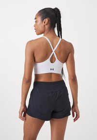Witte sportbeha met kruisbanden en een keyhole-detail, gecombineerd met zwarte shorts met een gelaagd ontwerp en een elastische tailleband.
