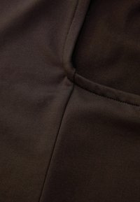 Brown stretch fabric with a smooth texture, featuring precise stitching and a subtle sheen. Includes a pocket on the side with a clean finish.