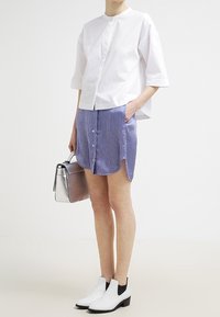 Vit kortärmad blus i kombination med en lila randig kjol med knappar. Svart- och vit randiga ankelstövlar; håller en metallisk silverväska.