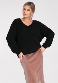 Schwarzer, flauschiger Strickpullover mit weitem Halsausschnitt, überschnittenen Schultern und langen Ärmeln, kombiniert mit einem hellrosa, seidigen Midikleid.