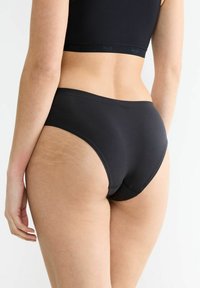 Schwarze Baumwoll-Hipster-Unterwäsche mit glatter Textur, die einen hohen Schnitt und nahtlose Kanten für minimale Sichtbarkeit unter der Kleidung aufweist.