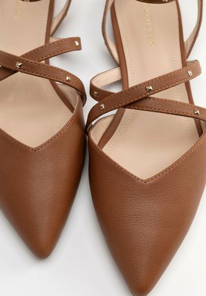 Bailarinas marrones de puntera puntiaguda con tiras cruzadas con pequeños tachones metálicos cuadrados sobre un fondo claro.