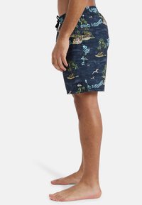 Patterned swim trunks in dark blue, featuring palm trees and islands, with a drawstring waist and a logo patch on the lower leg.