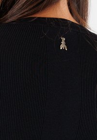 Top nero a coste con un pannello centrale liscio e una piccola spilla a forma di insetto in argento al colletto.