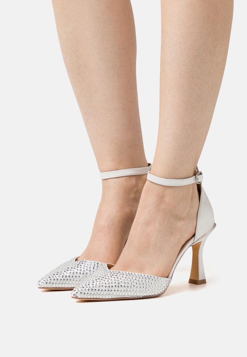 Chaussures à talons hauts argentées avec un bout pointu, une surface texturée cloutée et une bride à la cheville. Dotées d'un talon métallique pour plus de détails.