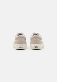 Pár béžových tenisek Vans zobrazených zezadu na bílém pozadí, se znakem "Off The Wall" na podrážkách.