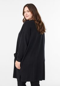 Must mustersuur kampsunkleit pikkade varrukate, soonikkoes mansettide ja küljetaskuga. Pehme kootud tekstuur, põlveni ulatuv disain.