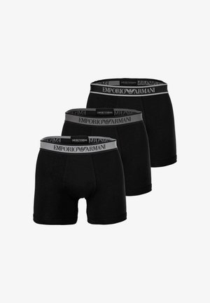 Trois boxers noirs pour hommes avec des ceintures grises ornées du logo Emporio Armani et de l'emblème d'aigle, disposés en formation décalée.