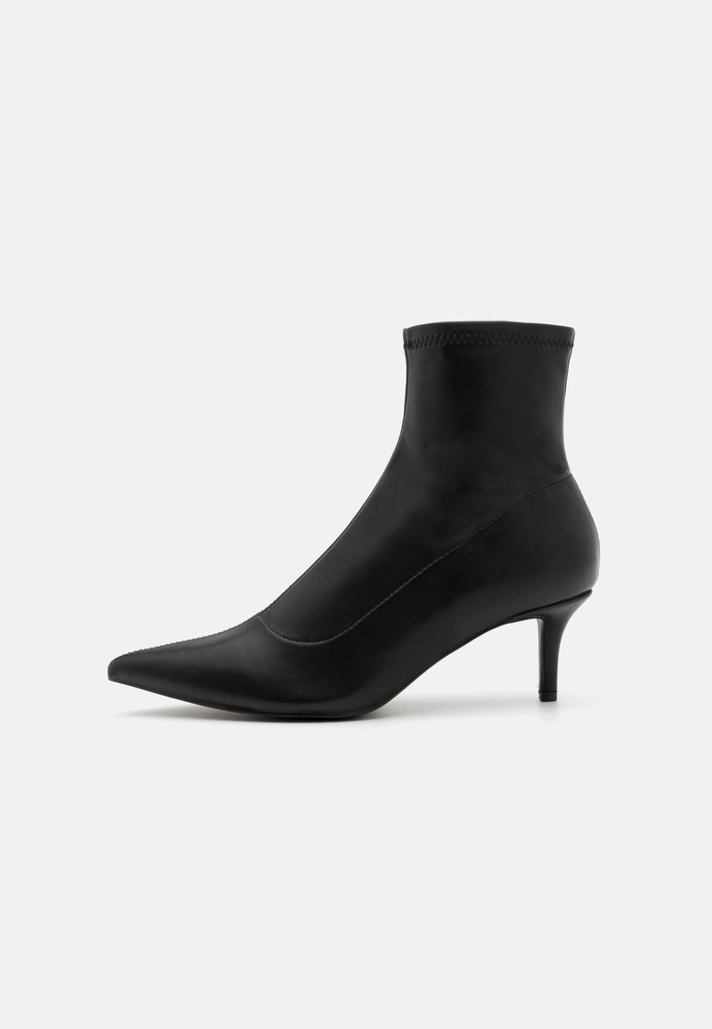 Bottine noire à bout pointu avec un talon de 5 cm. Fabriquée en matière lisse, elle présente un design sans couture et des détails de coutures discrètes.