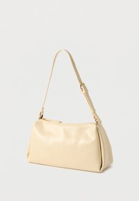 Sac d'épaule en cuir crème avec bandoulière ajustable et fermeture zippée sur le dessus, présenté sur un fond clair uni.