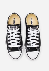 Paire de sneakers Converse All Star basses noires avec lacets blancs et bouts en caoutchouc, vues de dessus sur fond blanc.