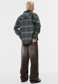 Sivá károvaná flanelová košeľa s dlhým rukávom, veľkým golierom a zadočkom, skombinovaná s širokými hnedými kordovými nohavicami. Minimalistický dizajn, textúrovaná tkanina.