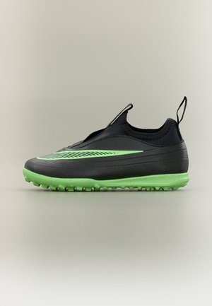 Čierna a zelená slip-on futbalová obuv s textúrovanou podrážkou a závesmi na päte a jazyku na neutrálnom pozadí.