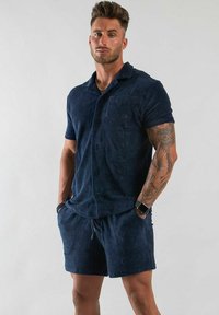 Mörkblå kortärmad skjorta med knappar och bröstficka, i kombination med matchande shorts, tillverkade av strukturerad tyg.