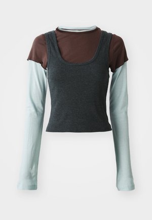 Gelaagde lange mouw top met een donkergrijze geribbelde cropped tank over een lichtblauw lange mouw basislaag en een bruin kort mouw shirt.