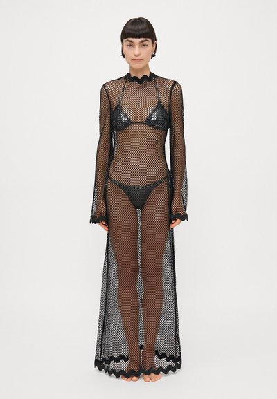 Couverture en maille noire avec des manches longues, un col festonné et un ourlet. Présente un design transparent sur un ensemble de bikini noir assorti.