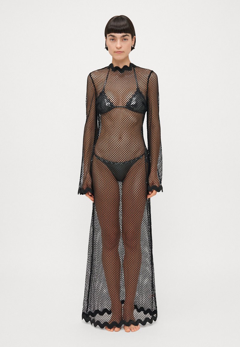 Couverture en maille noire avec des manches longues, un col festonné et un ourlet. Présente un design transparent sur un ensemble de bikini noir assorti.