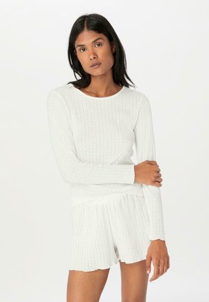 Weißes, geripptes Langarmoberteil mit rundem Halsausschnitt, kombiniert mit passenden Shorts mit gewelltem Saum. Sanfte Textur, minimalistisches Design.