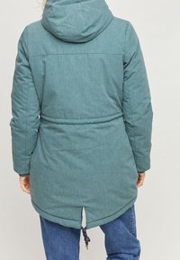 Giacca con cappuccio in blu teal, con vita stretta, maniche lunghe e orlo curvo; realizzata in tessuto testurizzato con un dettaglio di coulisse nella parte inferiore.