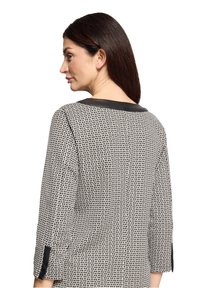 Zwart-wit top met patroon, gemaakt van een gestructureerde stof, met driekwart mouwen en een contrasterende zwarte halslijn.